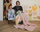 Christopher Farr Cloth’s Creative Director, Michal Silver, holding a sustainable patchwork quilt featuring the ‘Mikado’ embroidery in hot pink showing both front and reverse sides, with Véronique de Soultrait’s original artwork in the background.